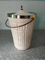 Full view of white plastic ice bucket with metal handle and lid attached, showing embossed geometric design and shiny metal rim.