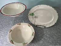 Three-piece set showing all items: oval platter with floral green design, oval bowl with red and black rim detailing, and round bowl with cut-out handles and green/brown rim accents.