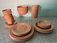 View of the full dish collection set arranged on kitchen counter, showing plates, bowls, cups, and pitcher in light brown plastic by Maplex.