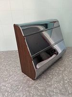 Side and front view showing the faux wood sides and reflective chrome front panel of the vintage kitchen roll holder.