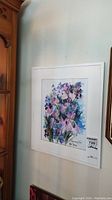 Framed watercolour painting by Angie Strauss hanging on a wall, showing the floral artwork and signature.