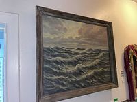 Framed oil painting showing turbulent ocean waves under a cloudy sky.