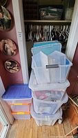 Stack of empty and filled plastic storage bins positioned near a closet with hangers inside.