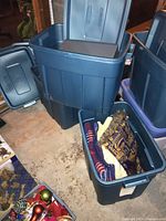 Wide angle photo showing three large blue plastic storage bins, one filled with blankets, the others with electronics.
