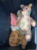 View inside one storage bin showing a large pink patterned teddy bear plush toy and other stuffed animals.