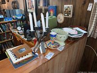 Photo of lot including candles, bowls, picture frames, and paintings arranged on wooden counter and mounted on wood-paneled wall.