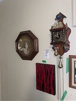 Wide view showing Dutch wall clock hanging above wool wall art and next to the framed collector plate.