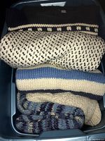 Overhead view of multiple folded men's sweaters in a plastic bin, showing different knit colors and patterns