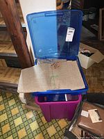 Blue plastic crate with primitive linen fabric folded inside, purple plastic crate underneath.