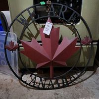 Front view of metal wall hanging with large red maple leaf and text WE ARE CANADIAN in black metal frame.