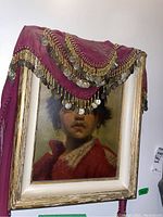 Photo of framed oil painting with pink belly dancer scarf draped over top corner, showing frame condition and scarf details.