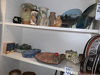 Shelves filled with multiple pottery items including vases, plates, figurines, and ceramic containers.