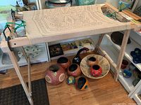 Front view of wooden weaving stand holding a woven frame sample; metal clamps and green bungee cords attached.
