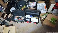 Photo showing two open tool boxes filled with various hand tools and supplies next to rubber boots and a boxed item.