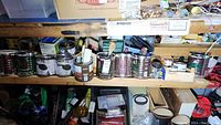 Wide view of top shelves with assorted paint cans, containers, and hand tools scattered along the shelf edges.