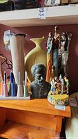 Wide view of lot showing tall beige ceramic vase, large yellow ceramic vase, Tsjaikofsky bust, Venus figure sculpture, music box, and pencil holder