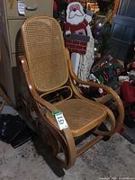 Front angle view of vintage wooden rocking chair with cane seat and backrest, showing curved armrests and rocker base.