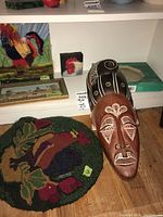 Four pieces of wall art and accessories on shelf including hooked rug rooster art, two carved masks, and boxed mold.