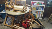 Overall lot showing tabletop loom parts on table, spinning wheel behind, warping board to left, tool bag underneath