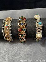 Photo showing all three chunky vintage bracelets on a black display: one gold-tone mesh with turquoise and faux pearls, one gold-tone linked chain with multicolored stones, and one silver-tone with faux pearls and floral rhinestones.