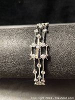 Close-up of 3 strand bracelet showing clear round stones and metal links on black display tube.