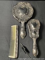 Vanity set showing handheld mirror, hairbrush, comb, and three bobby pins laid out on a black background.