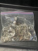 Ziplock bag filled with various silver tone jewelry pieces visible, including rings, hoop earrings, bracelets, some bent or broken.