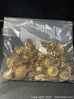 Plastic zip bag filled with assorted broken or incomplete gold-tone jewelry including earrings, decorative pendants, and charms with pearl accents