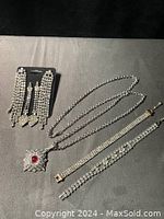 Overview of lot: two pairs of rhinestone dangle earrings on card, one long necklace with red stone pendant, two bracelets with rhinestones