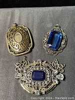 Top view of all three pendants on gray background showing cobalt blue stones in varied ornate metal frames for crafting use.