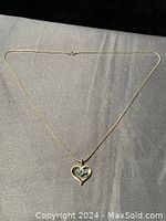 Full view of the gold-tone necklace with heart pendant featuring blue stones, lying flat on a black surface.