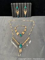 Handmade native jewelry set arranged with earrings on a black stand, and bracelet and necklace laid flat on a black surface