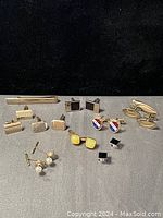 Photo showing various cufflinks and a tie clip arranged on gray fabric against black background for clear detail.