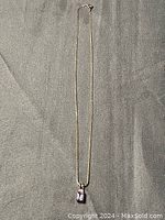Full view of gold tone chain necklace with amethyst-like pendant laid on gray fabric background.
