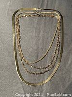 Top-down view of four gold tone chains arranged on a dark surface showing different chain links and lengths