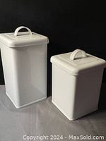 Pair of two white enamel metal boxes, one taller rectangular and one shorter square, with lids shown on top