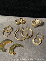 Six pairs of vintage gold-tone hoop earrings of varying sizes and styles on grey background.