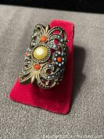 Photo of women's fashion ring size 6.5 with filigree metalwork and colored stones on red ring holder