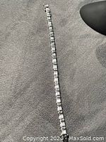Full length of the tennis bracelet laid out on a textured gray surface showing its length and design.