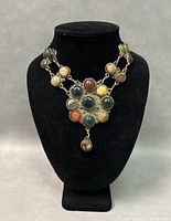 Front view of amulet necklace with detailed views of multicolored stones and metal links on black jewelry display.