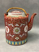 Side view of red porcelain teapot with Chinese floral and shou motifs, spout, and woven handle.