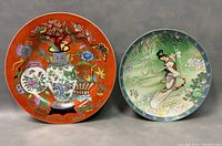 Two decorative Asian plates, one orange with vases and flowers, one green with an Asian woman and mountain scenery