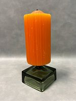 Side view of green glass square candleholder with original tall orange ribbed candle inserted upright.
