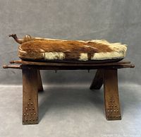 Side view of the wooden camel saddle stool showing the camel head carving and fur seat.