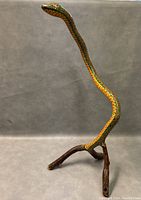 Front angle of hand painted wooden snake sculpture with colorful patterns and natural wood base.