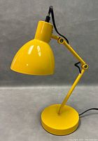 Yellow Luminaire adjustable desk lamp with bent arm and round base set against a grey background.