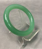 Close-up angled view of the smooth green jade round bangle bracelet on a clear display stand.
