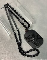 Full view of natural black obsidian bead necklace with rectangular hand carved wolf pendant shown on a clear display stand.