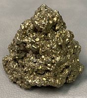 Photo of first raw pyrite stone showing metallic gold cubic crystals on irregular surface.