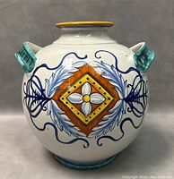 Front view of round Italian ceramic jar with hand painted floral and geometric designs, twin handles, and yellow rim.